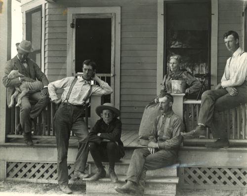 historic photo of a group of 6 people sitting and standing on a porch